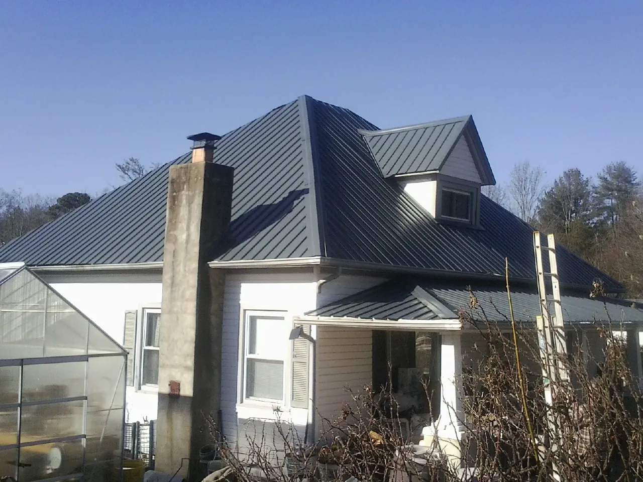 Dark blue standing seam metal roof on a white farmhouse with dormer — Slate & Tile Roof Repair by Roofing Brothers in Naples