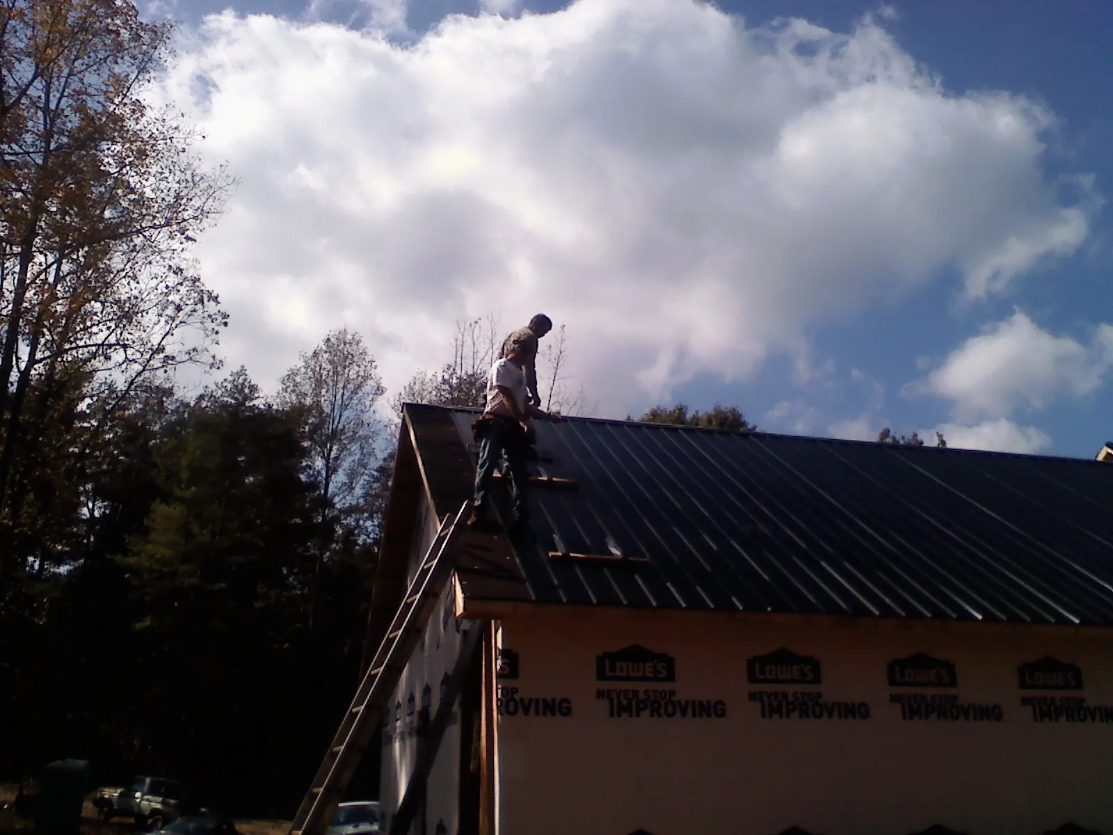 Roofer fastening dark metal panels high against a cloudy sky, from a Roof Inspection job in Naples